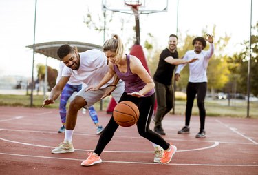 Group of multiracial young people   playing basketball outdoors