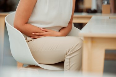 Closeup of one mixed race business woman holding stomach because of pain during menstrual cycle