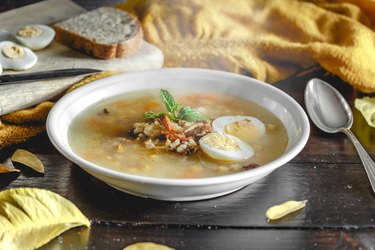 Healthy and warming winter soup with rice, chickpeas, chicken, ham and boiled egg over rustic wooden table background. Spanish soup (Puchero Andaluz). Winter food concept