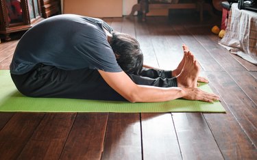 person in a t shirt and pants with short hair does seated forward fold on a green yoga mat