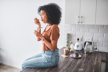 Woman eating yogurt on kitchen counter