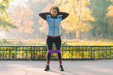 Person outdoors in workout clothes at the top of a squat demonstrating the start of a kang squat