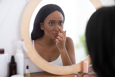 woman looking at her nose in the mirror because she has a pimple inside her nose