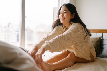 年轻的亚洲女人在早上伸展双腿躺在床上