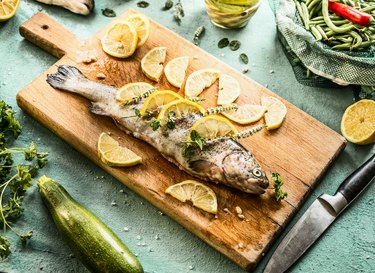 Raw vitamin D-rich trout fish on cutting board stuffed with herbs and lemon slices