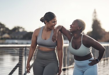 who women laughing after an outdoor workout, wearing sports bras and tights