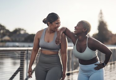 two athletes laughing after an outdoor workout wearing sports bras and tights