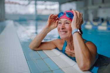 Happy senior woman in swimming pool, leaning on edge.