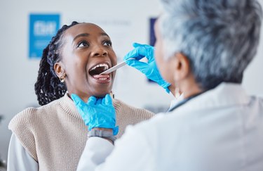 a person with long black braids holding their mouth open while a doctor examines their cracked tongue