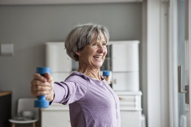 senior woman wearing a purple sweater and lifting blue dumbbells at home