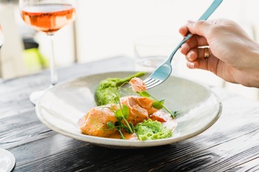 Close up of a hand holding a forkful of baked salmon with pea puree