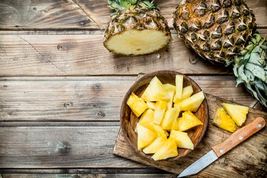 Pieces of fragrant pineapple in a bowl on a cutting Board with a knife.