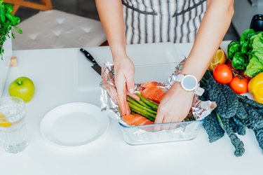 Hands preparing vegetables and salmon dish on white kitchen counter as a method for how to reduce waist size from 36 to 32