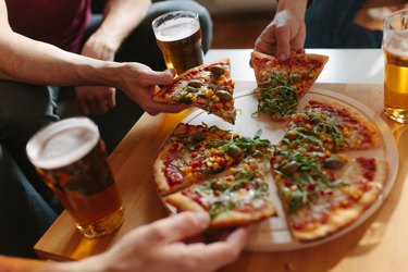 A group of people eating pizza and drinking beer, as an example of foods that irritate hiatal hernia