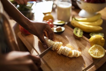 close view of a person cutting up a banana on a wooden cutting board