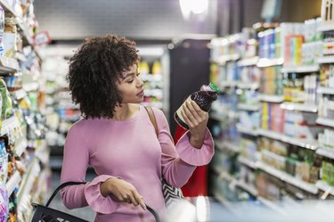 Young woman shopping in supermarket, looking at the nutrition facts label to calculate her percent daily value of fiber.