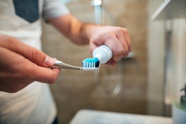 Close-up of person squeezing SLS-free toothpaste on a toothbrush, as a natural remedy for canker sores