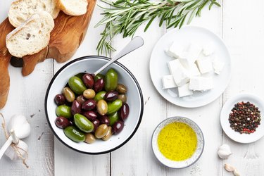 Bowl of Olives and Cubed Cheese With Olive Oil Peppercorns Garlic and Bread over wooden background