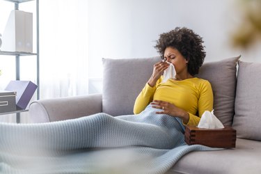 Woman sneezing in a tissue in the living room.