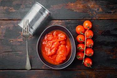 overhead photo of peeled canned tomatoes and fresh tomatoes on old dark wooden table