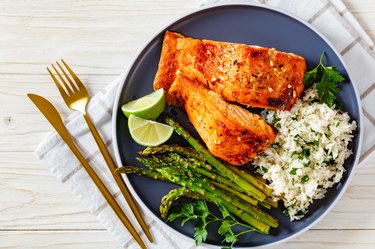 Salmon fish fillet with rice and asparagus on blue plate on white wooden table