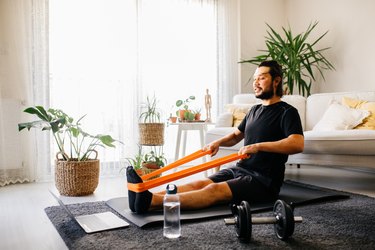 man doing seated resistance band exercises on the floor of  his living room, watching a computer