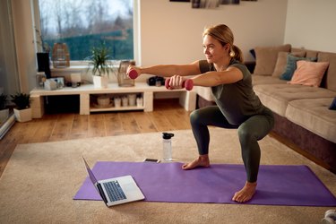 woman doing dumbbell squats on a purple yoga mat in her living room