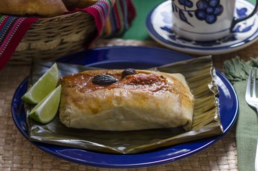 traditional Guatemalan tamales baked in the oven on a blue plate on top of corn husk with lime wedges