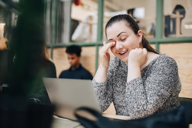 Smiling businesswoman rubbing eyes while using laptop on desk in office