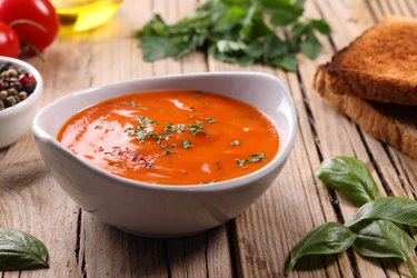 Tomato Soup cooked with frozen tomatoes on wooden board with basil