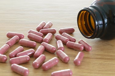 A bottle of cranberry pills scattered on a wooden table, to represent herbal medicine for UTI