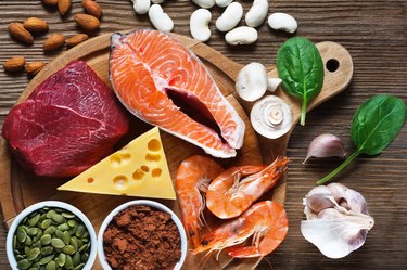 overhead shot of foods high in zinc like salmon and red meat with shrimp and cheese on wooden cutting board