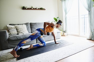 Woman working out with dumbbell in living room of home, doing dumbbell back exercises