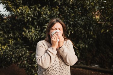 woman standing outside and blowing her nose because her allergies are getting worse with age