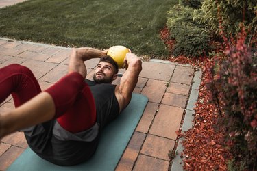 男人穿着背心和紧身裤做kettlebell ab锻炼在瑜伽垫