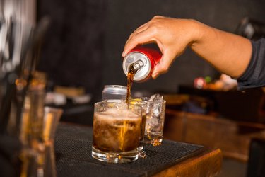 a person pouring a can of soda into a glass, as an example of food that contains calcium disodium edta