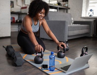 Person sitting on exercise mat working out at home with kettlebells to demonstrate a seated kettlebell workout.