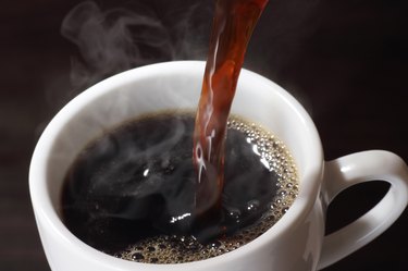 overhead photo of coffee pouring into a white mug with a black background