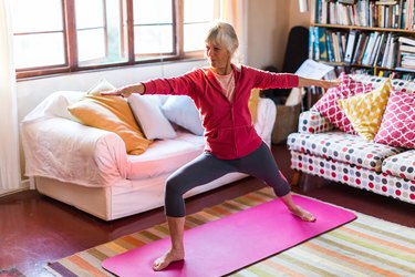 Older adult with gray hair in a ponytail doing yoga for menopause on a pink mat in the living room