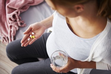 Top view of pregnant person holding glass of water in one hand and fiber supplements in the pregnancy category in the other hand