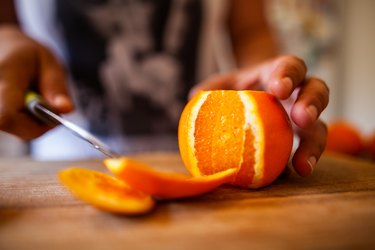 close view of a woman cutting an orange, one of the foods to avoid during allergy season