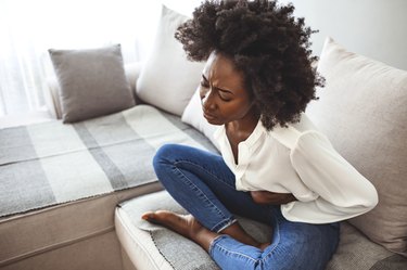 Woman Sitting On Sofa holding her stomach in pain