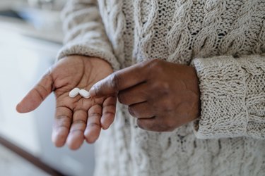 A person wearing a chunk off-white sweater holding two white immune-boosting supplements in their hands