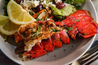 Prepared Lobster Tail from a frozen pre-cooked lobster on a white plate with lemon wedges and Greek salad