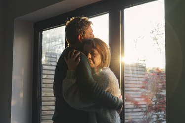 Close-up of a couple hugging each other while standing in front of a window as an example of how to help someone with depression