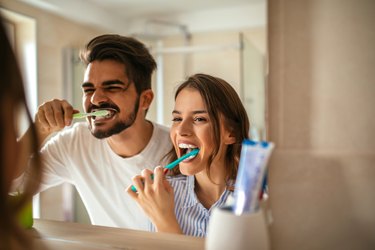 couple brushing their teeth in the bathroom mirror