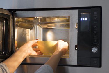 a person putting a bowl of food into a microwave, to represent the best snack before bed for sleep