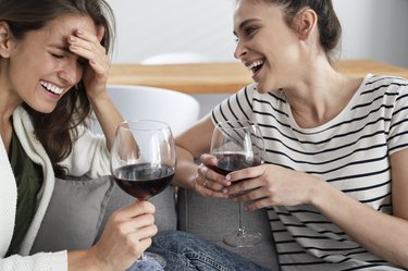 Two friends laughing with a glass of wine in hand