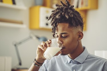 a Black man drinking a glass of milk at home, to demonstrate lactose intolerance by race