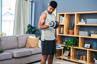 Person wearing gray tank top and black shorts doing a biceps curl with dumbbell in living room.